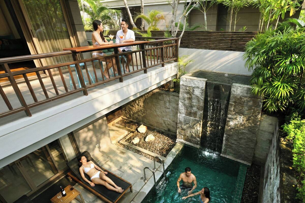 Un área de piscina con cascada, sillones de descanso y una terraza de madera.