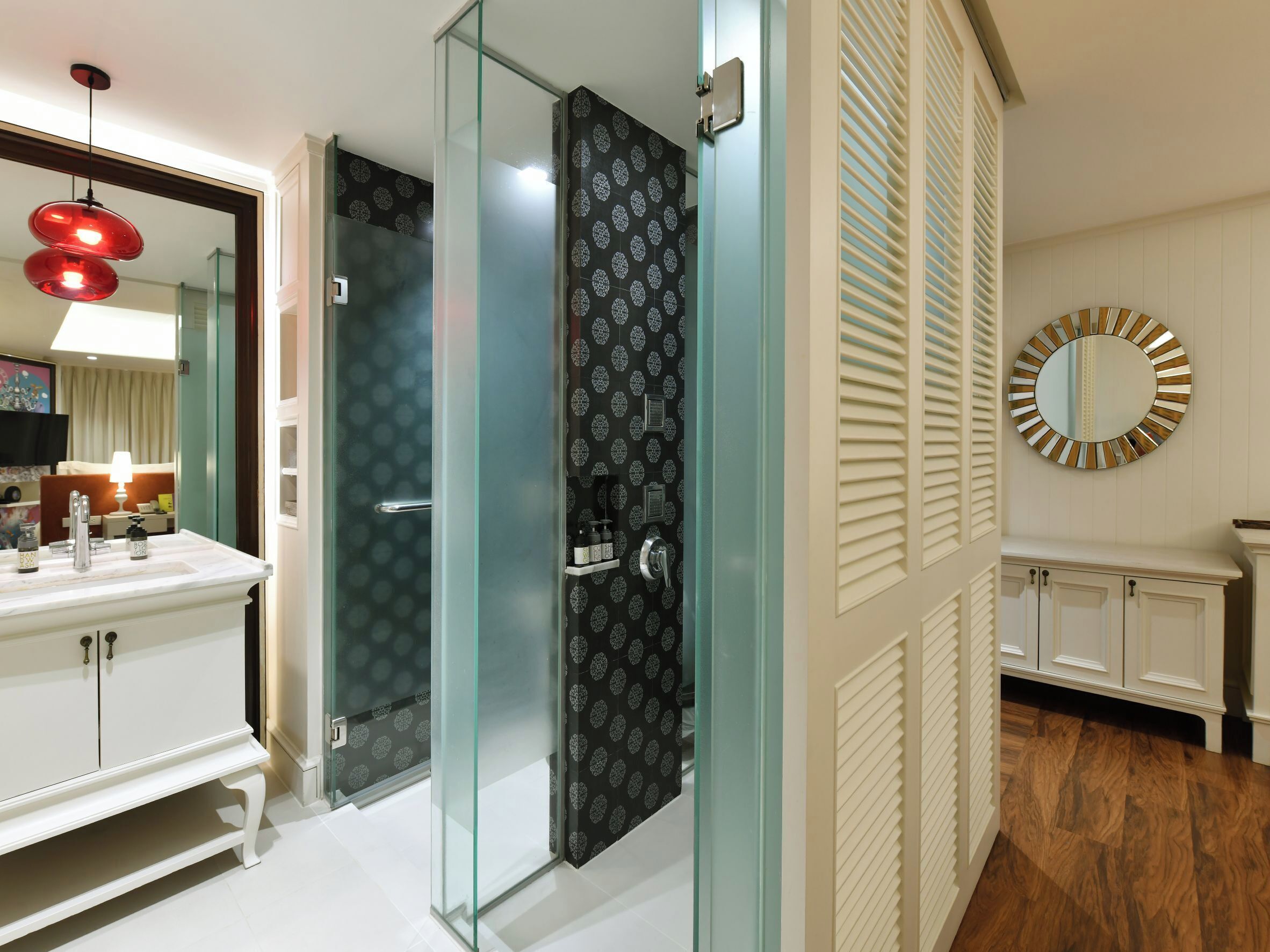 A modern bathroom with a glass shower enclosure, a white vanity with a mirror, and a round mirror on the wall.