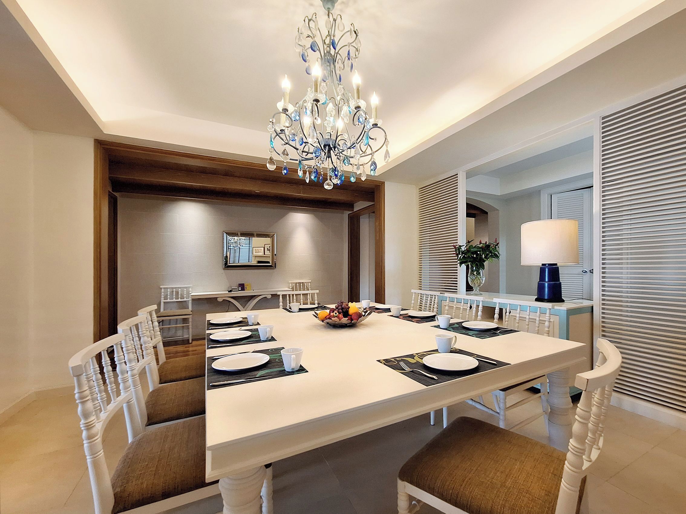 A dining room with a chandelier, a long table, chairs, and a mirror on the wall.
