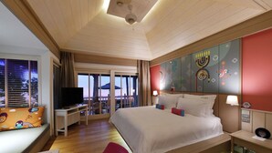 Ein Hotelzimmer mit einem großen Bett, einem Fernseher, einem Schreibtisch und Blick auf den Strand.