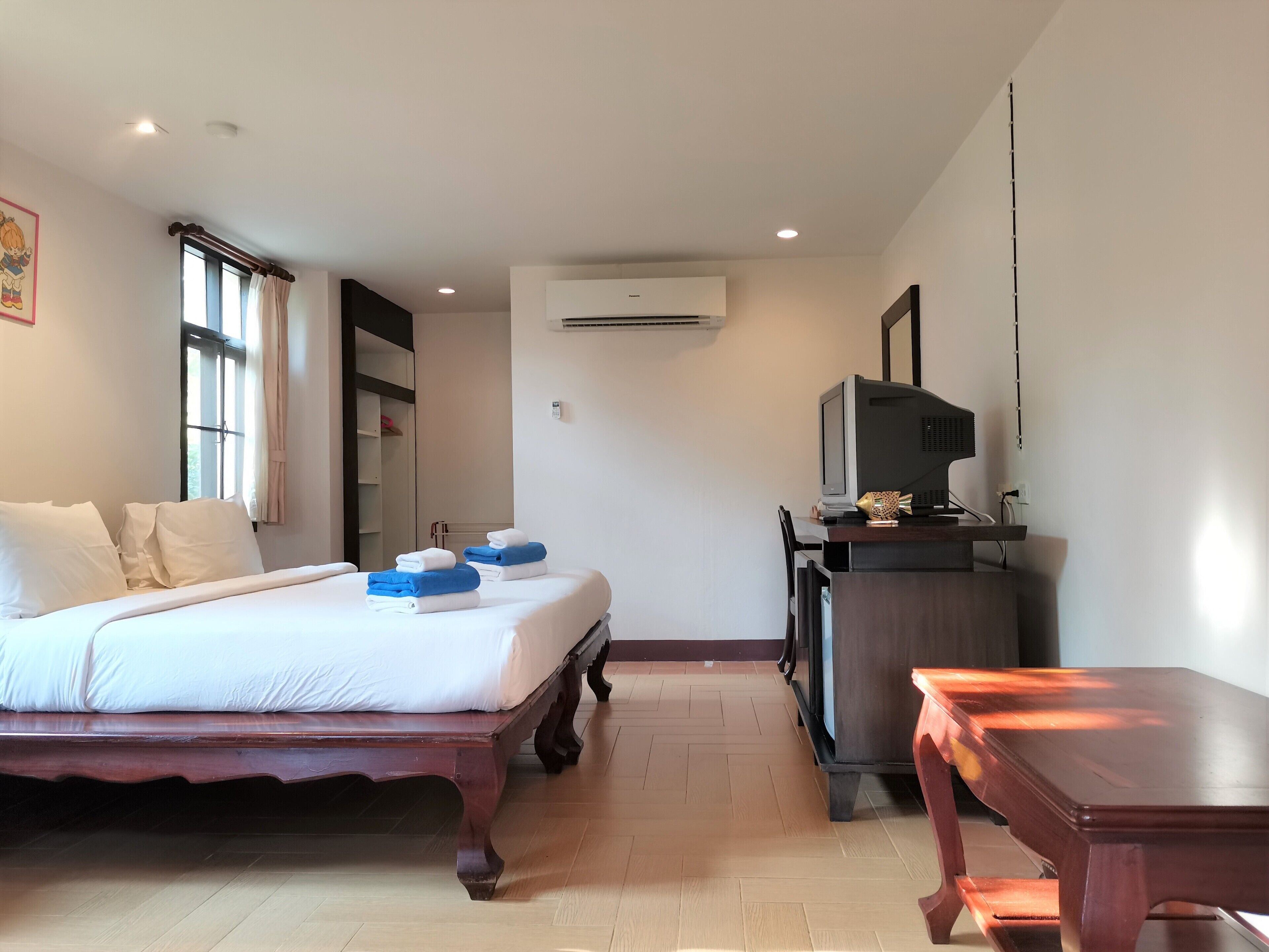 A hotel room with a bed, a desk with a computer, and an air conditioning unit.