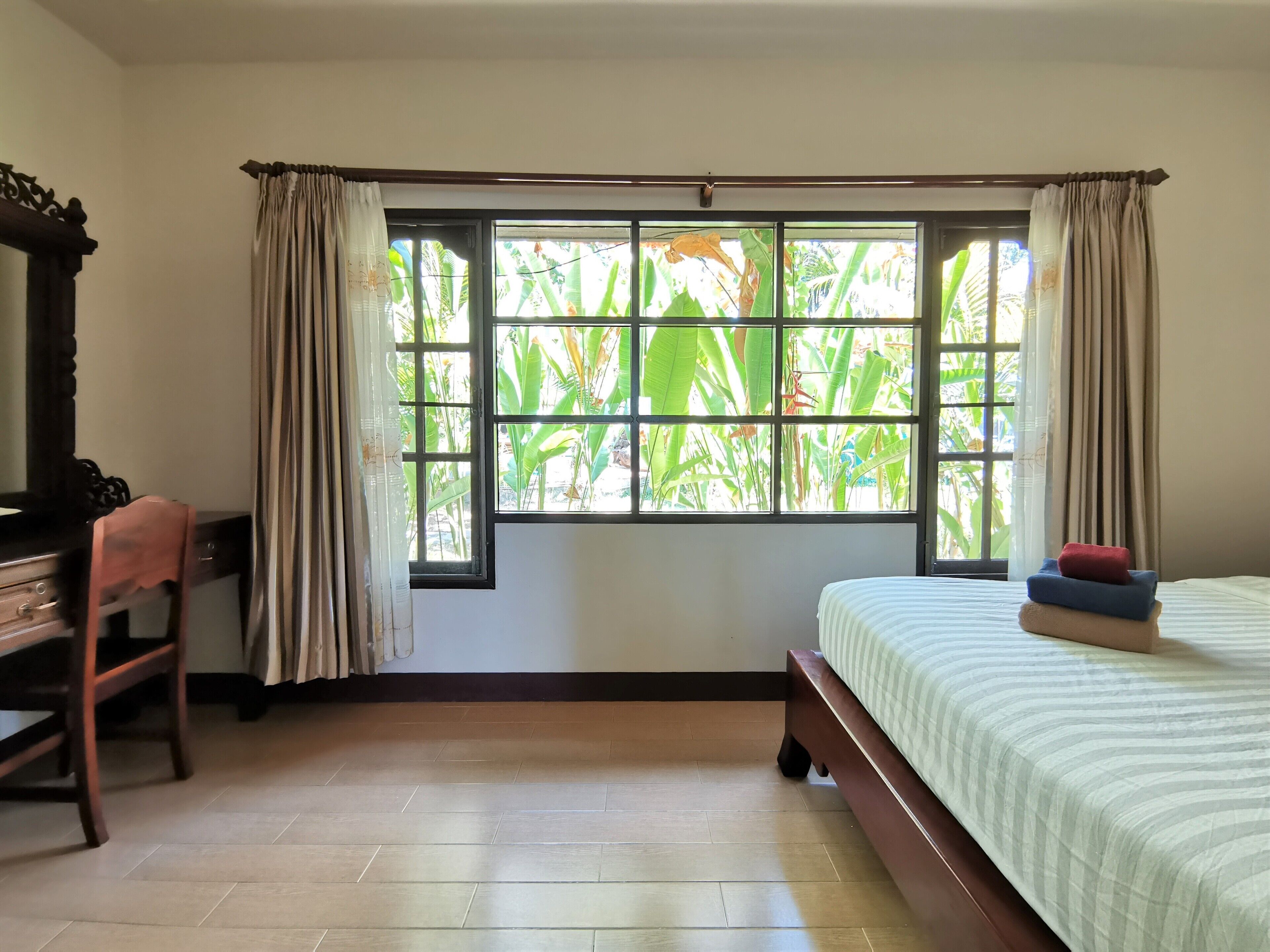 A bedroom with a bed, a desk, and a window with curtains.