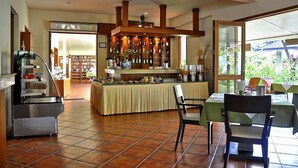 Un restaurante con área de bar, bufé y comedor con mesas y sillas.