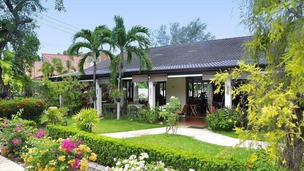Una casa con porche cubierto, rodeada de jardines cuidados y palmeras.