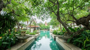 Ein ruhiger, überdachter Pool mit gefliestem Boden, umgeben von üppiger Bepflanzung und traditioneller Architektur im Hintergrund.