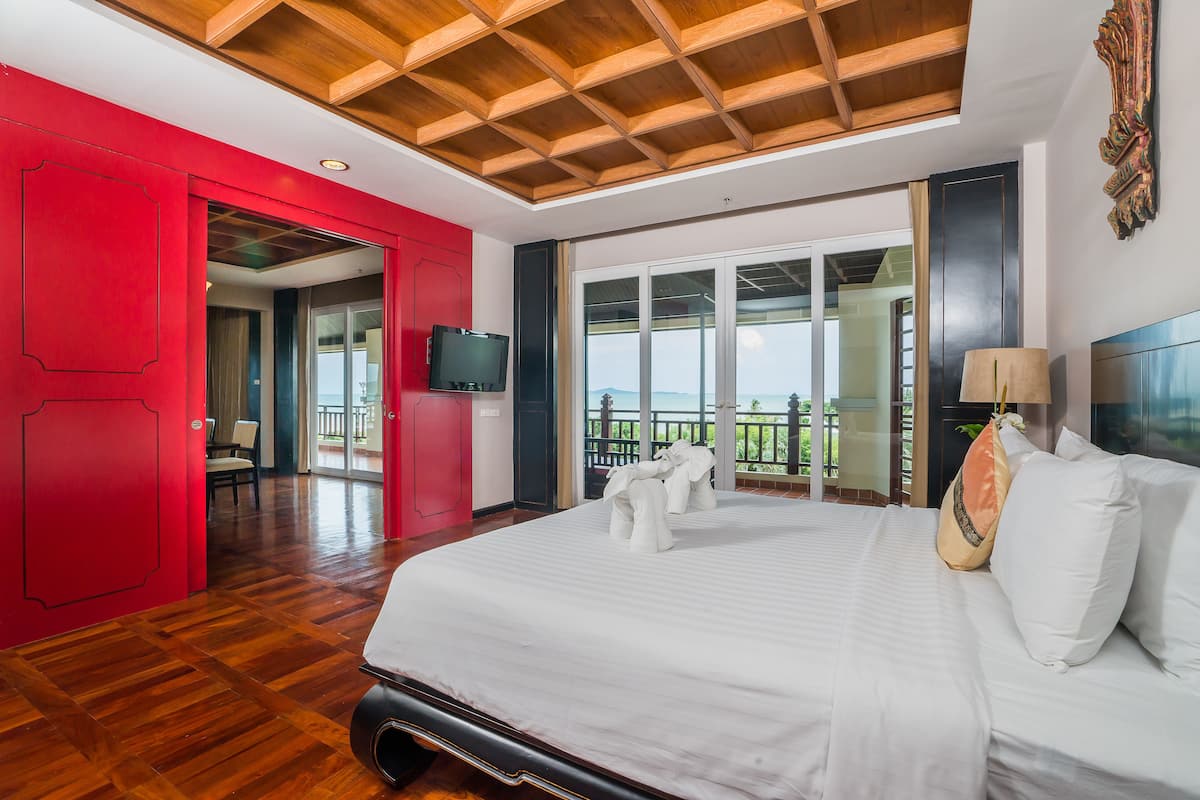 Ein Hotelzimmer mit einem großen Bett, einem Fernseher, einem Balkon mit Blick und einer roten Wand.