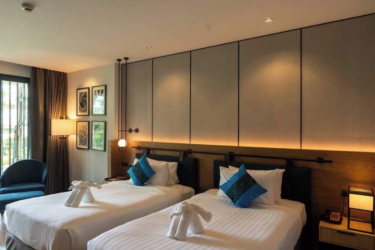 Ein Hotelzimmer mit zwei Betten, einem Schreibtisch, einem Stuhl, einer Lampe und einem Fenster mit Vorhängen.