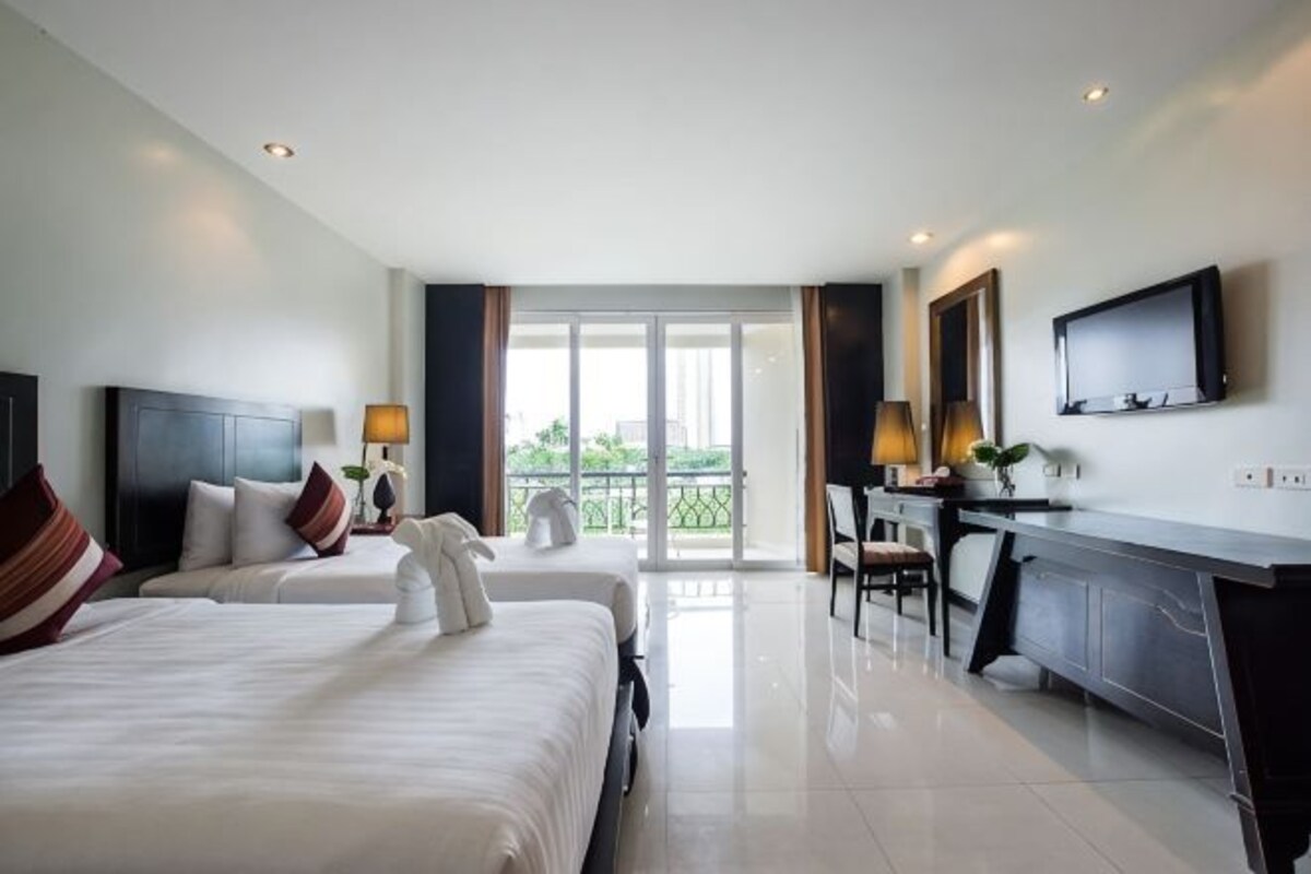 A hotel room with two beds, a desk, a television, and a balcony with a view.