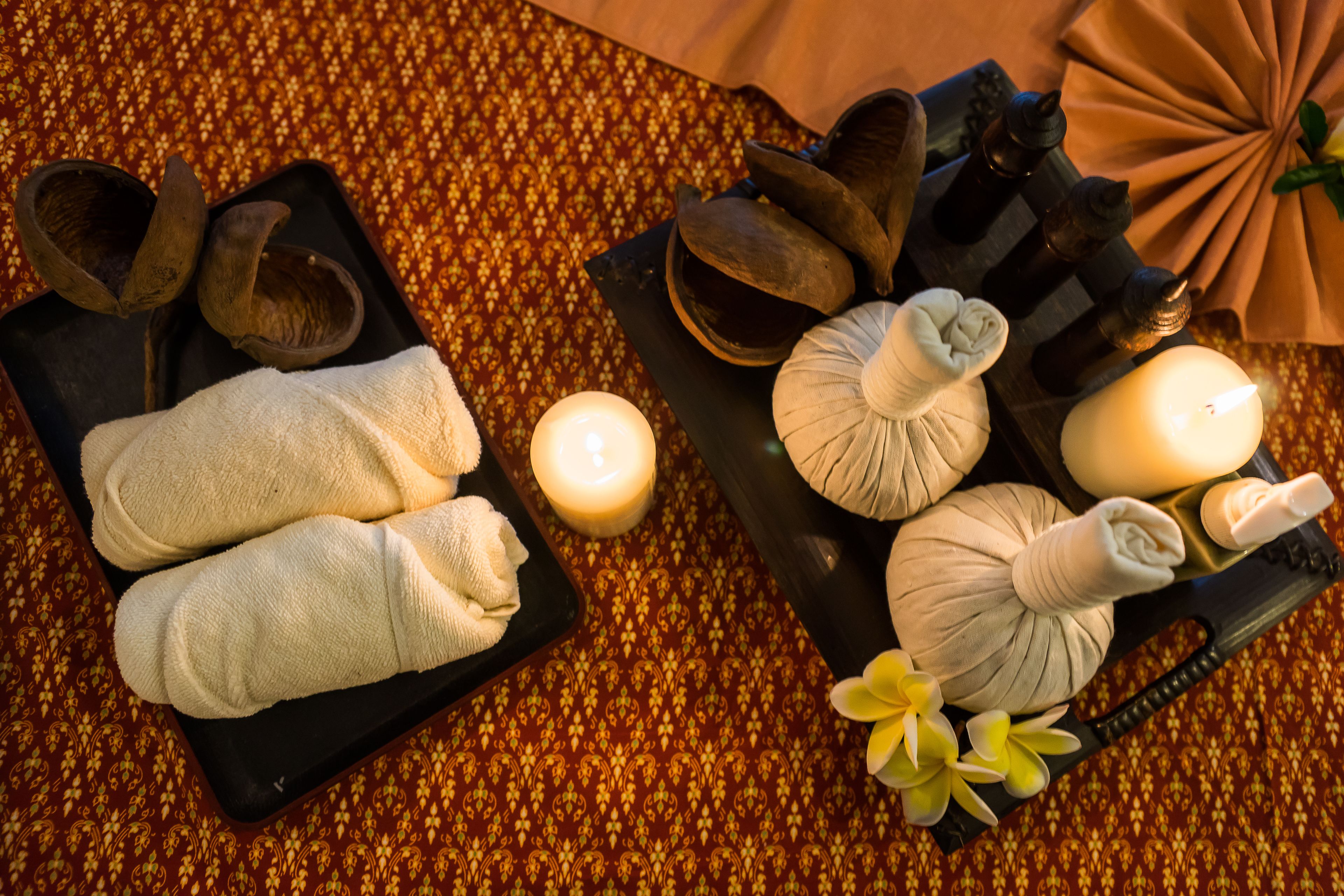 Un espace de bien-être avec des serviettes, des bougies et des accessoires de massage disposés sur une table à motifs.