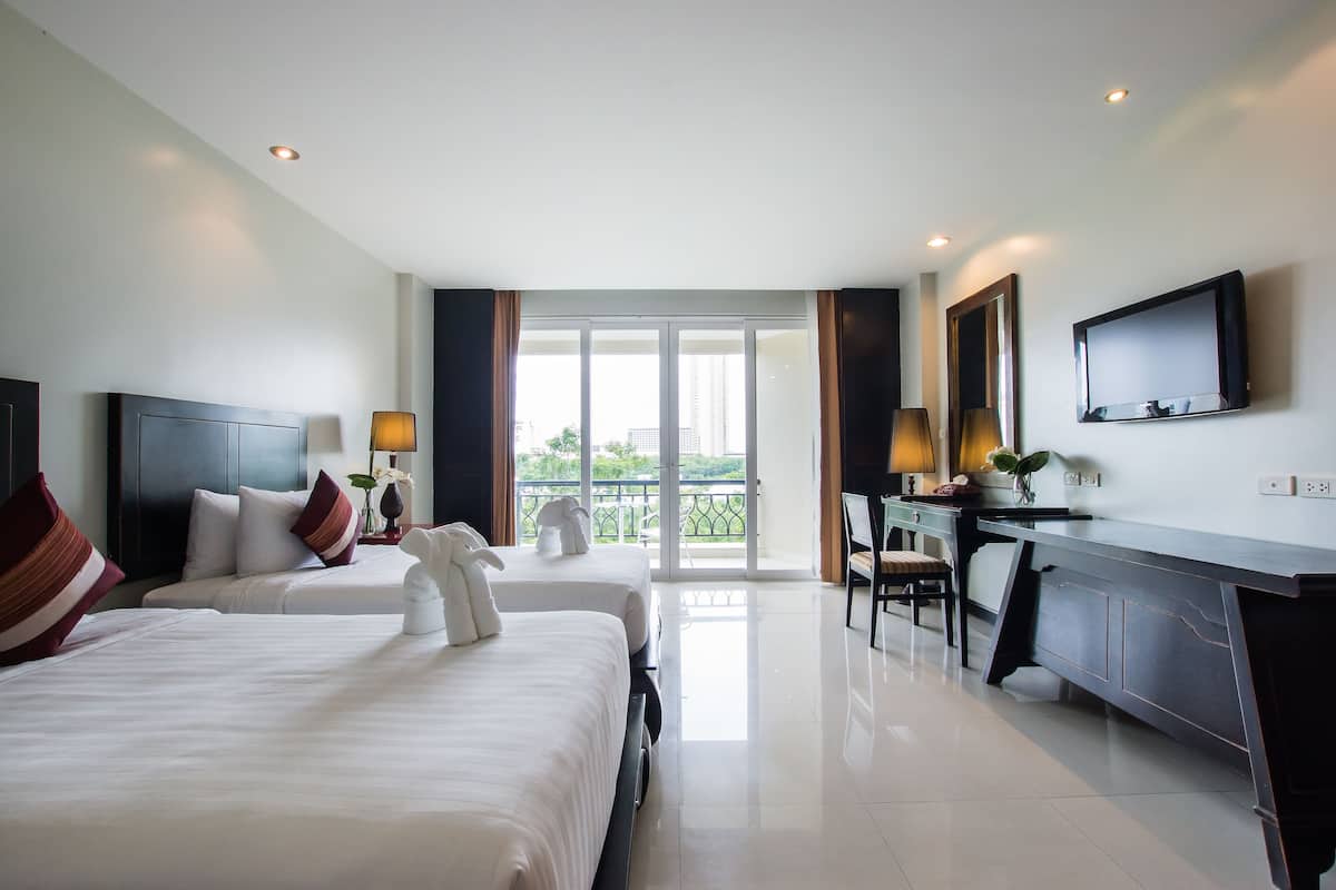Ein Hotelzimmer mit zwei Betten, einem Schreibtisch, einem Stuhl, einem Fernseher und einem Balkon mit Blick.