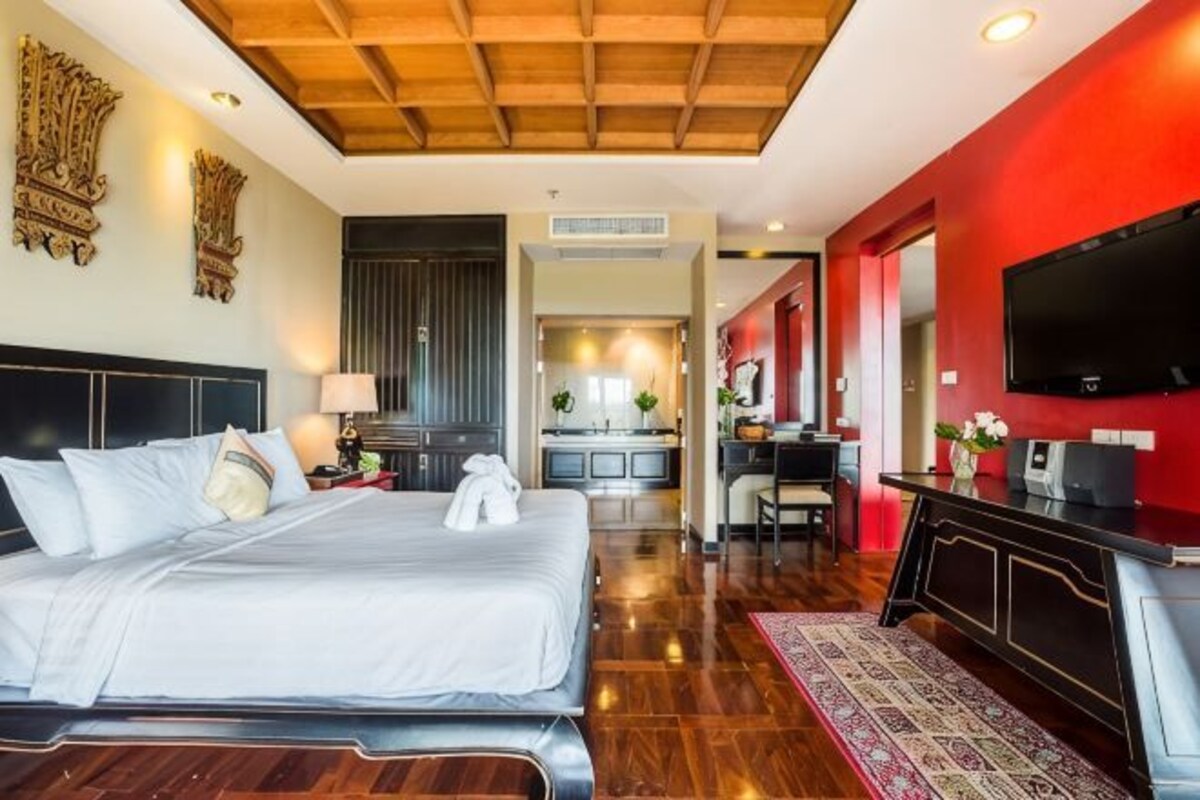 A hotel room with a bed, a TV, a desk, and a kitchen area.