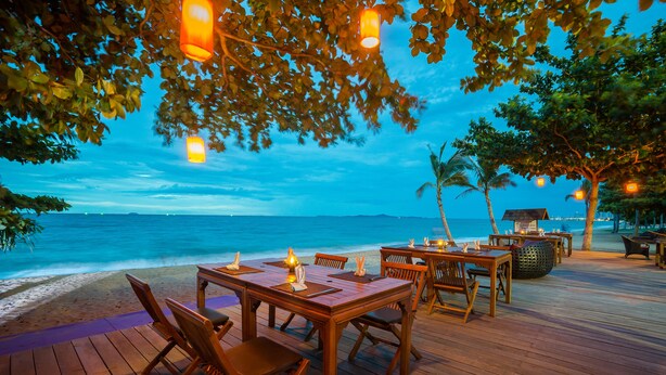 Eine Holzterrasse mit Tischen und Stühlen, mit Blick auf einen Strand und den Ozean.