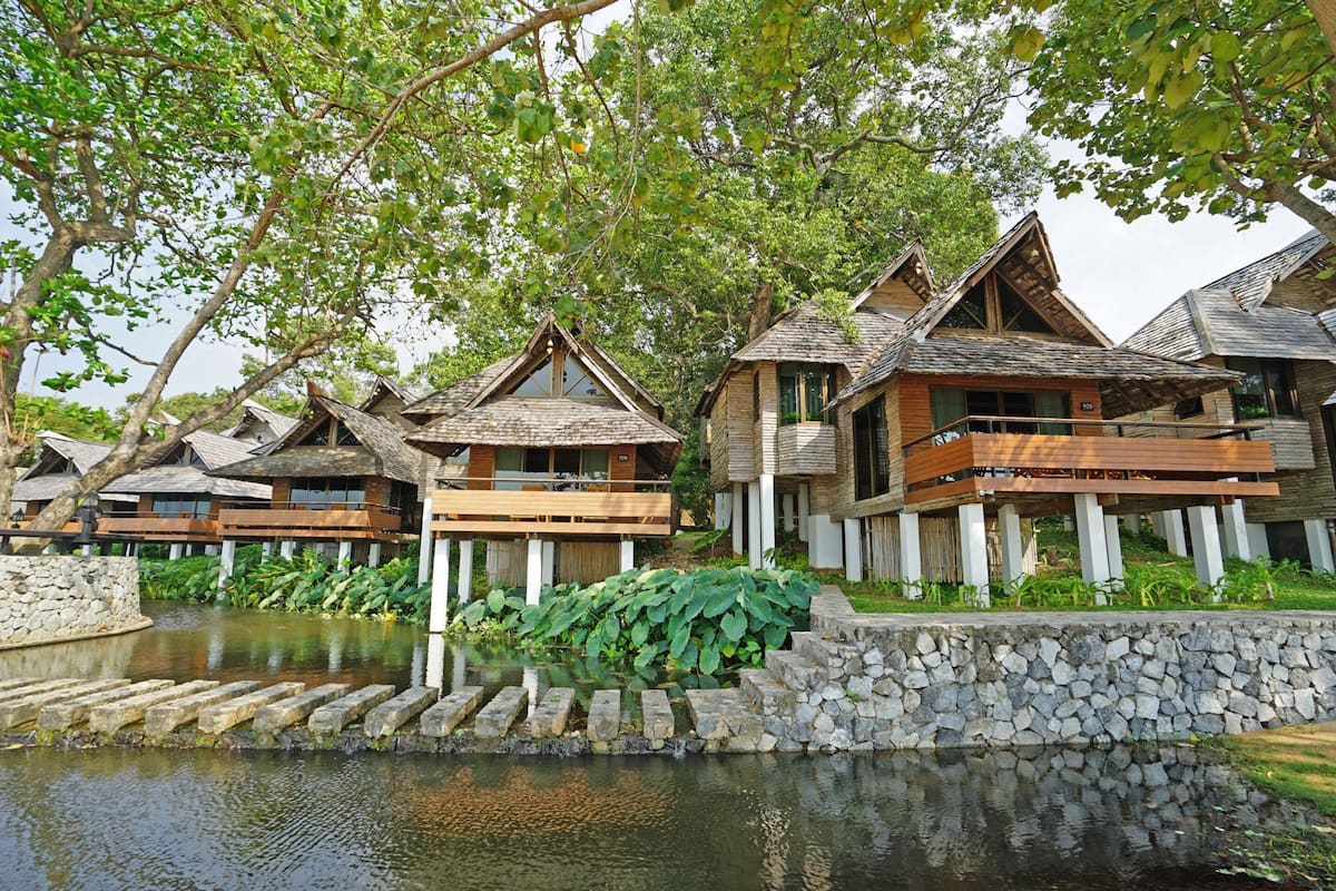 A row of wooden cabins with balconies, a stone wall, and a water feature.