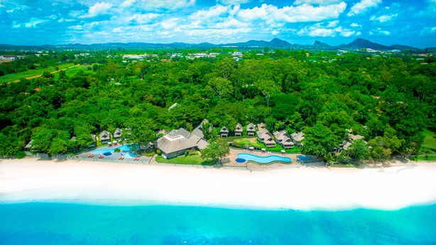 Vista aérea de un complejo turístico con varias cabañas, una piscina y una playa.