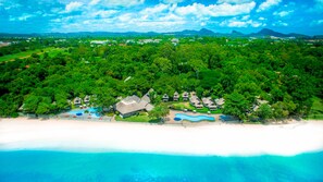 Vue aérienne d’un complexe hôtelier comprenant plusieurs bâtiments de style bungalow, une piscine et une plage.