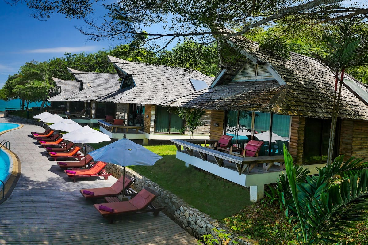 A pool area with lounge chairs and umbrellas, overlooking the sea.