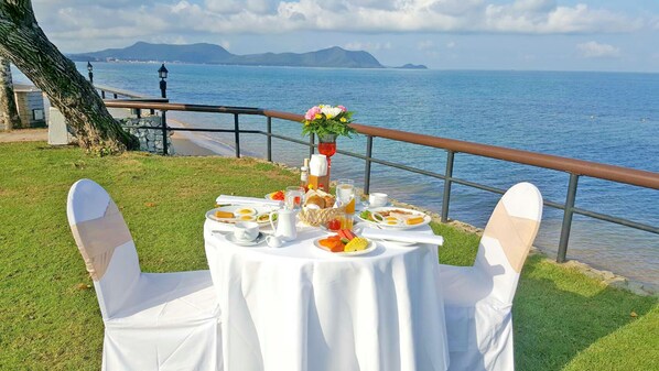 Une table dressée pour le petit-déjeuner, avec une vue sur la mer et les montagnes en arrière-plan.