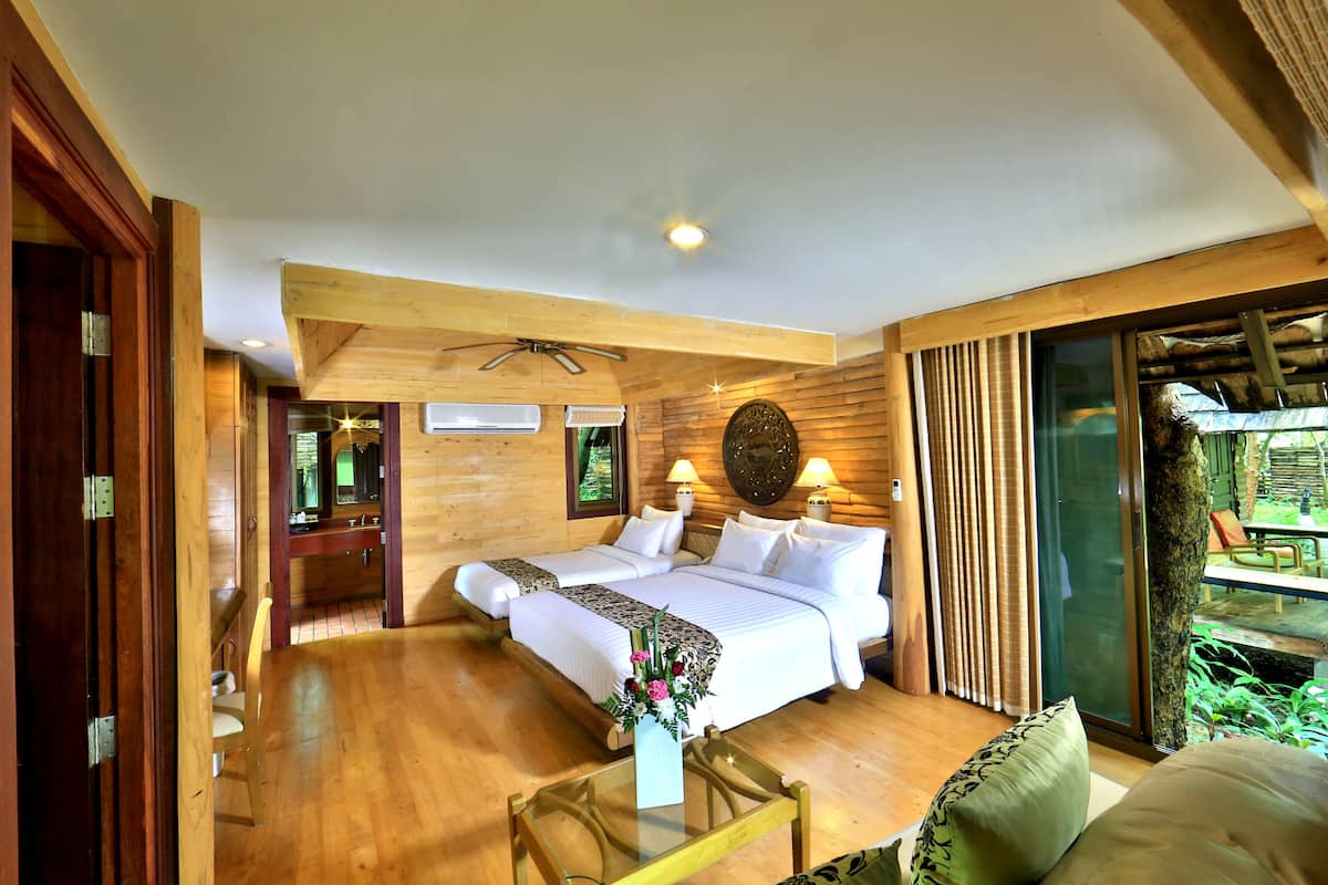 A wooden-themed bedroom with two beds, a glass coffee table, and a view of the outdoors.