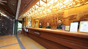 Una recepción con mostrador de madera, techo con diseño geométrico y cartel que indica 