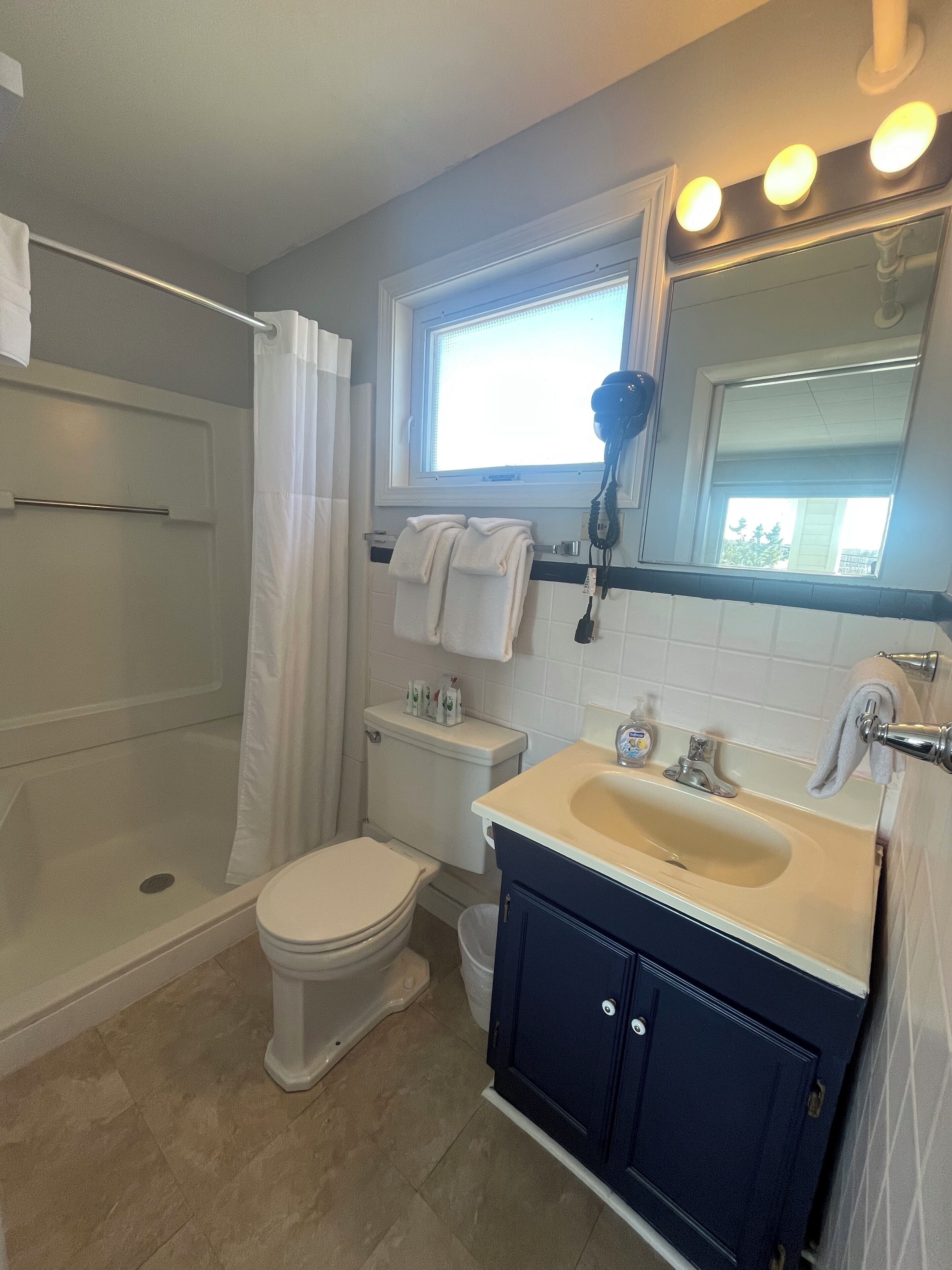 A bathroom with a bathtub, toilet, sink, and a window with lights above the mirror.