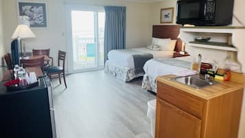 A hotel room with a kitchenette, a dining area, and a bed with a view of the outside.