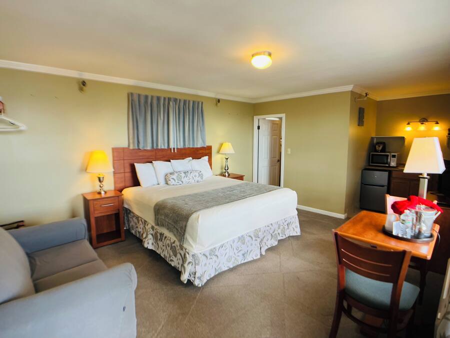 A hotel room with a bed, bedside tables, a desk, a chair, a microwave, and a refrigerator.