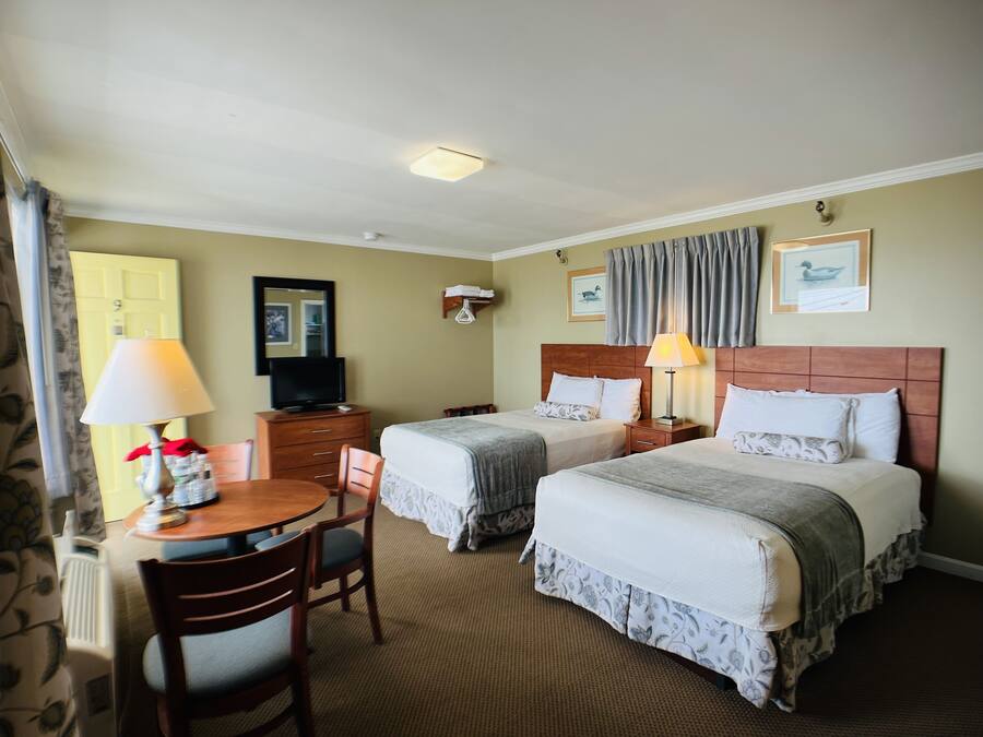 A hotel room with two beds, a desk with a chair, a television, and a dining table.