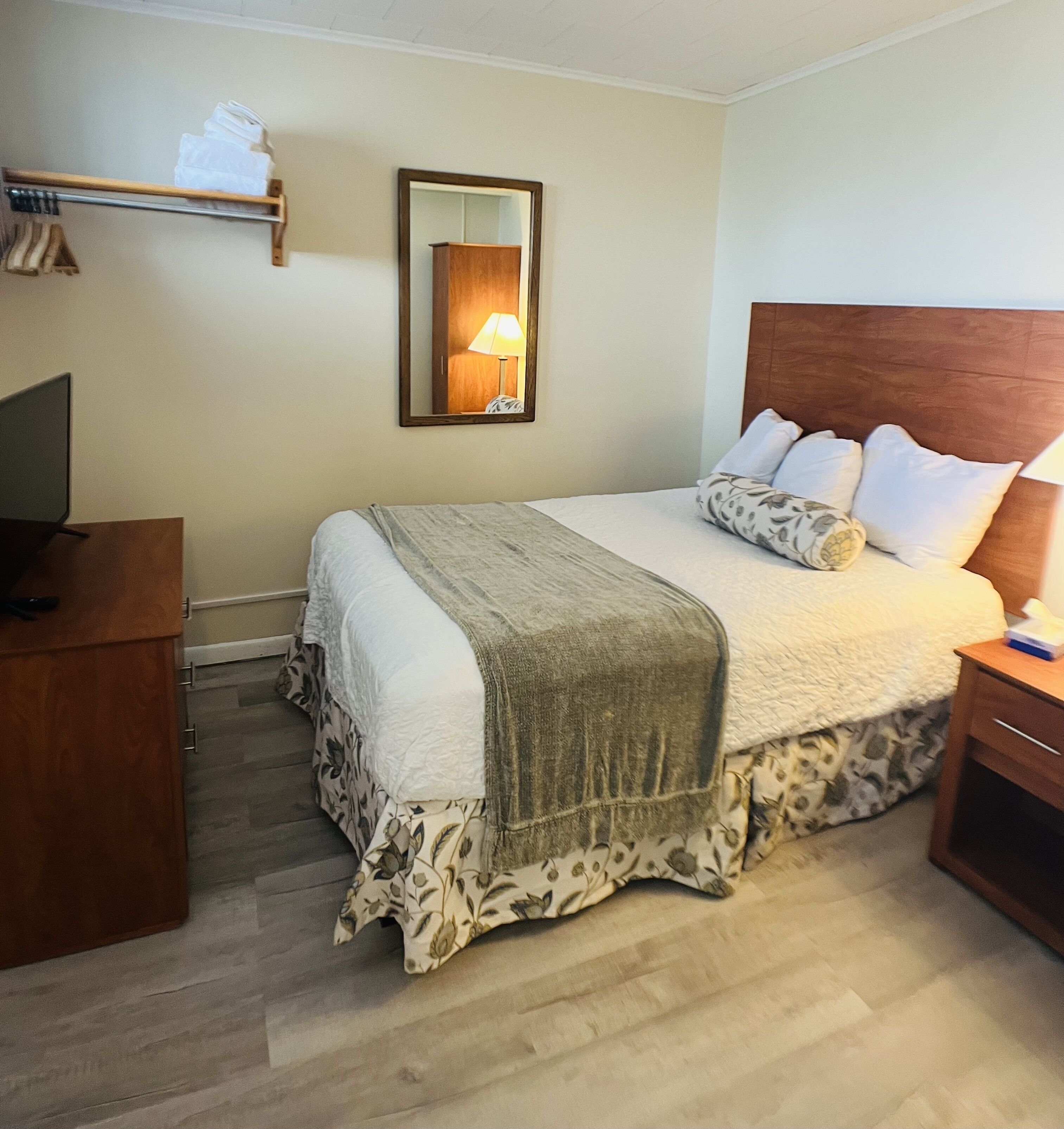 Ein Hotelzimmer mit Bett, Nachttisch, Lampe, Spiegel und Fernseher auf einem Schrank.