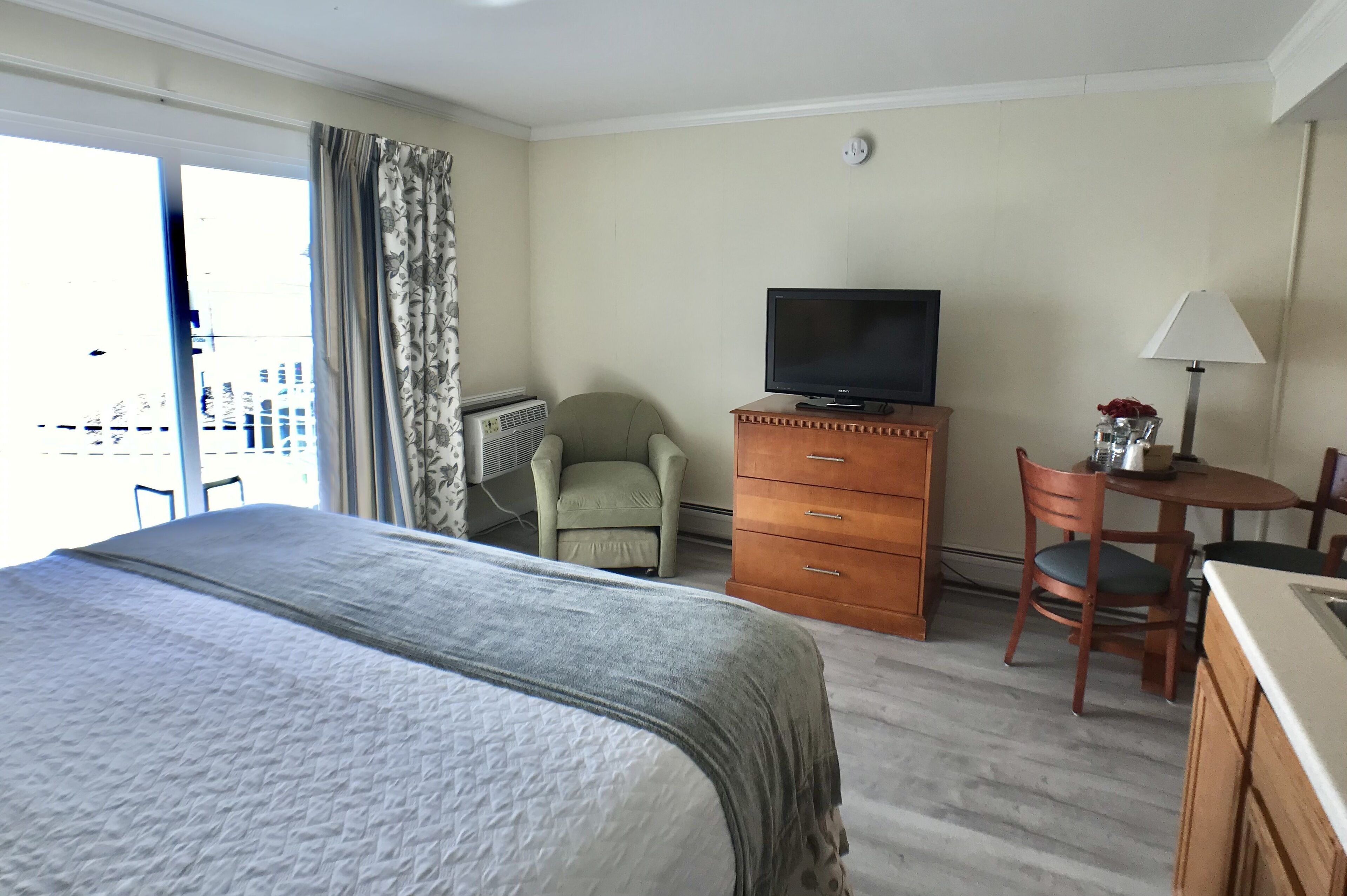 Une chambre d’hôtel avec un lit, une télévision, un bureau avec une chaise, une lampe et une vue sur la ville par la fenêtre.