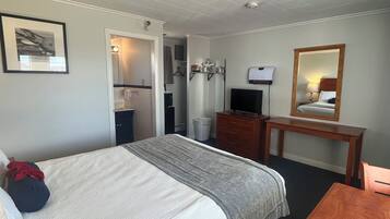 Habitación de hotel con cama, escritorio, espejo, televisor y baño visible a través de una puerta abierta.