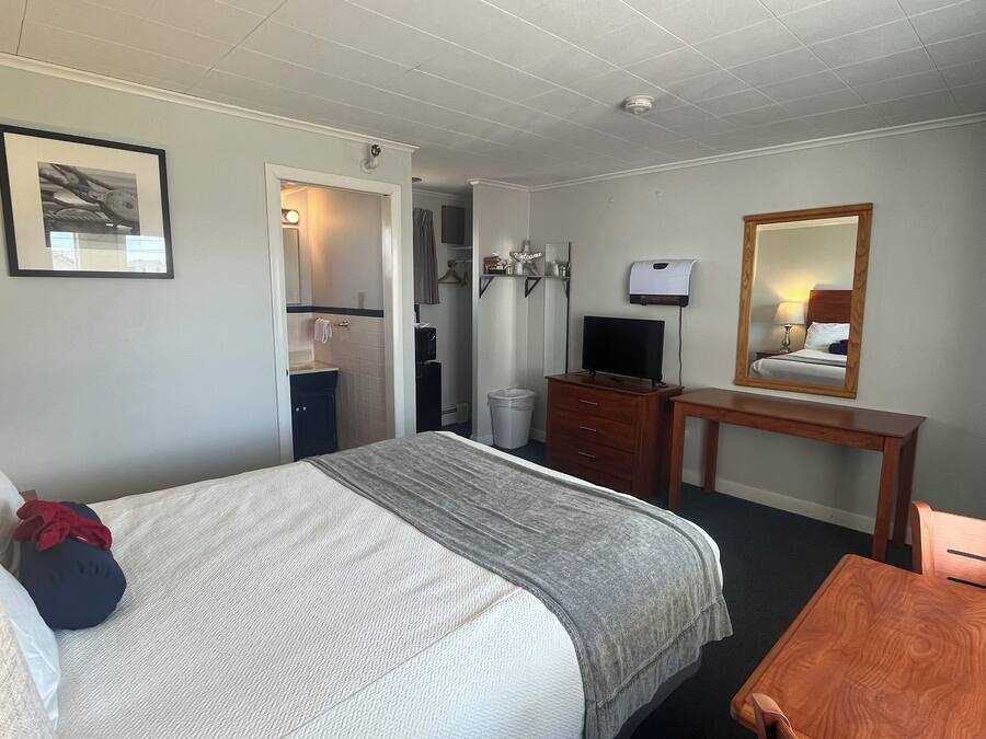 Habitación de hotel con cama, escritorio, espejo, televisor y baño visible a través de una puerta abierta.