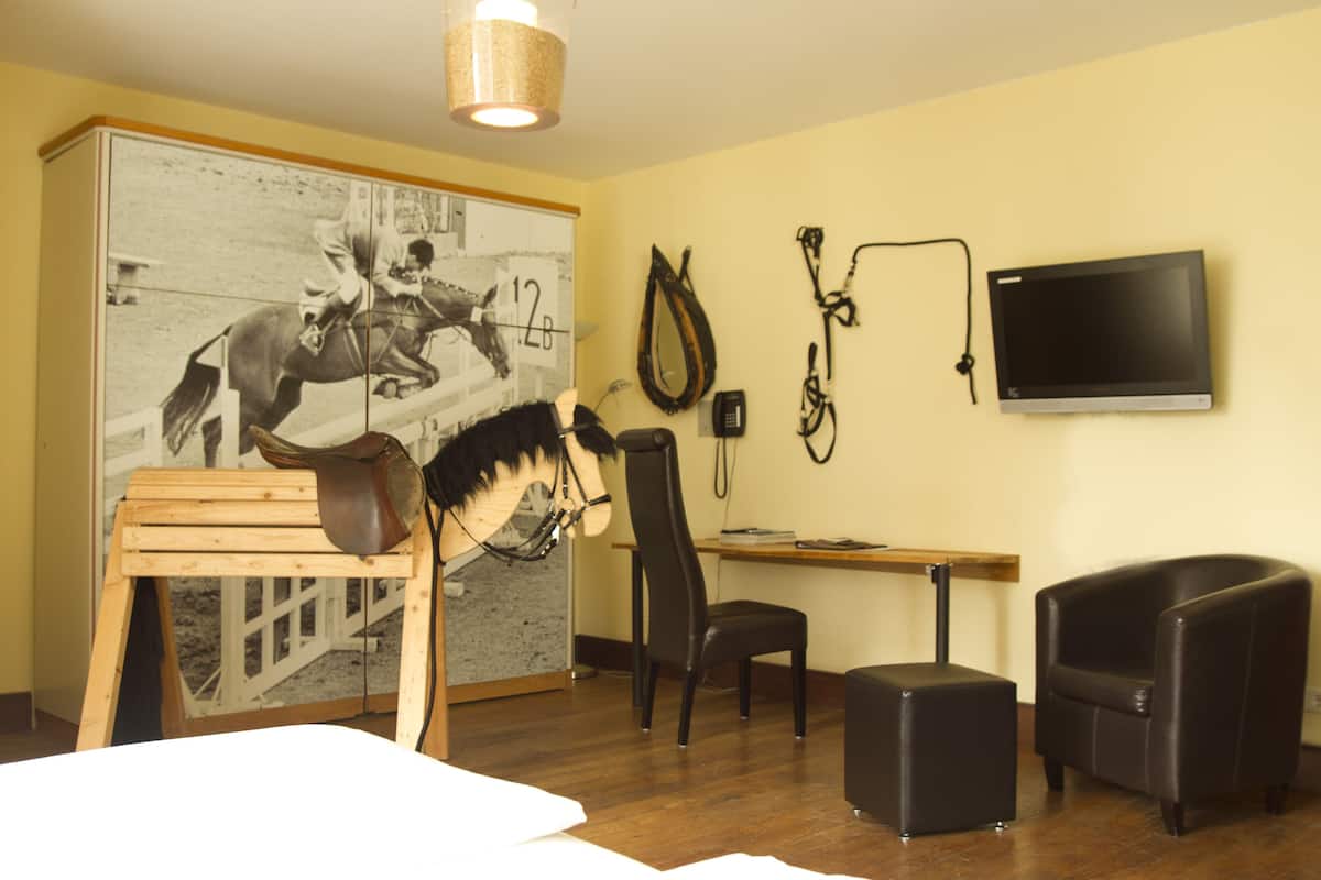 Une pièce comprenant un téléviseur fixé au mur, une affiche représentant un cavalier, une table en bois, un fauteuil en cuir et un bureau.