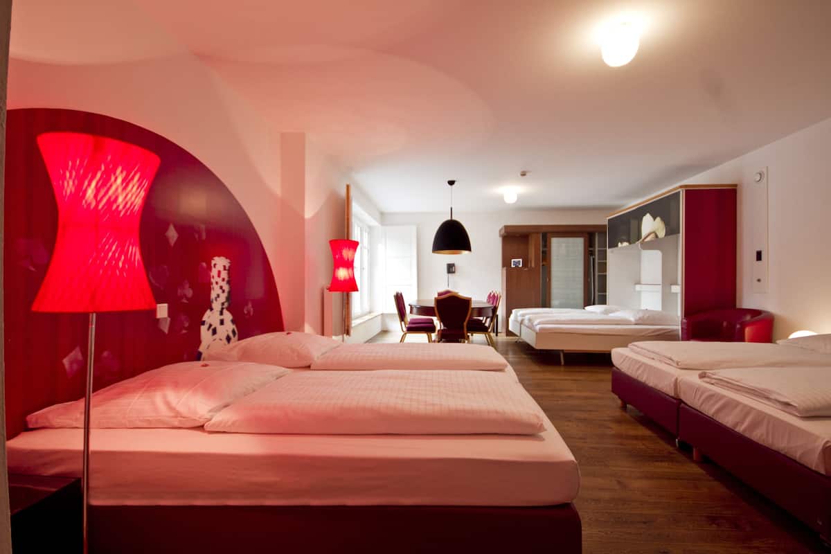 Une chambre d’hôtel avec deux lits, un coin repas et un mur d’accent rouge.