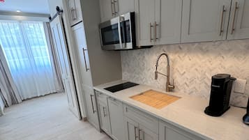 A modern kitchen with grey cabinets, a built-in microwave, a sink with a wooden cutting board, and a coffee machine.