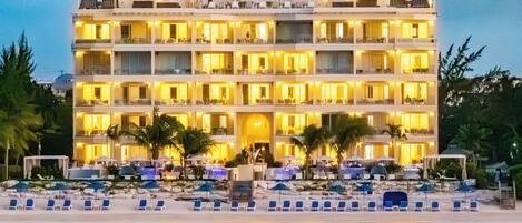 A multi-story hotel with balconies, a poolside area with lounge chairs, and a beach view.