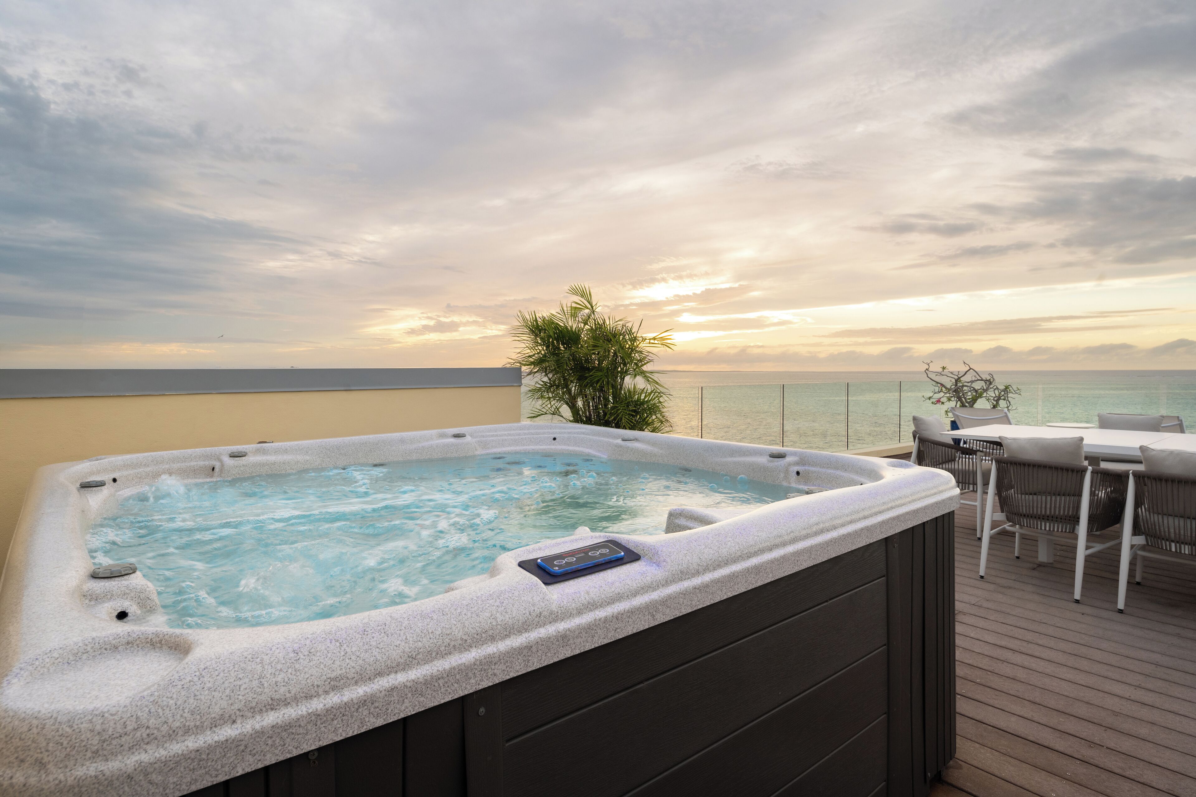 A hot tub on a deck with a view of the sea and a sunset.