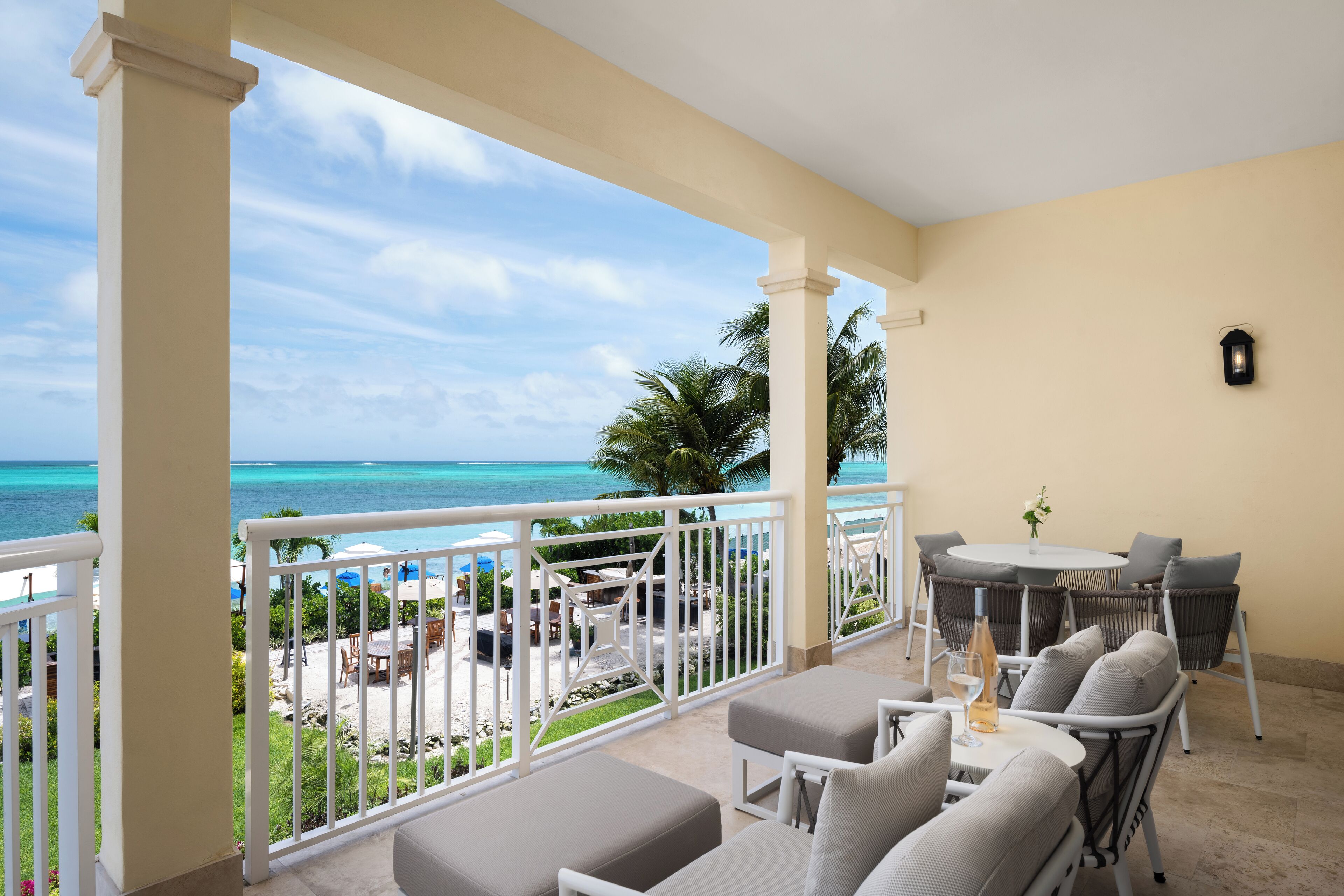 A balcony with a view of the ocean, outdoor furniture, and a table with a vase of flowers.