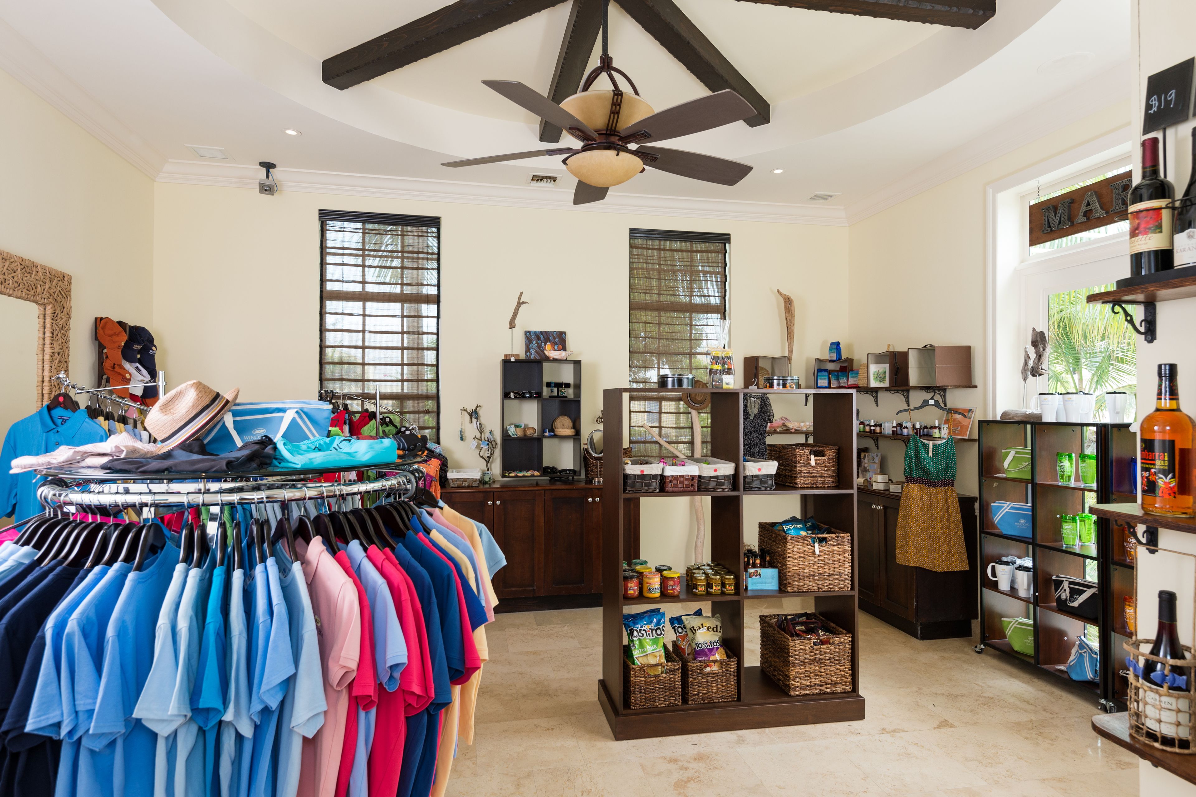 A spacious room with a clothing rack, shelves with bottles, and a ceiling fan.