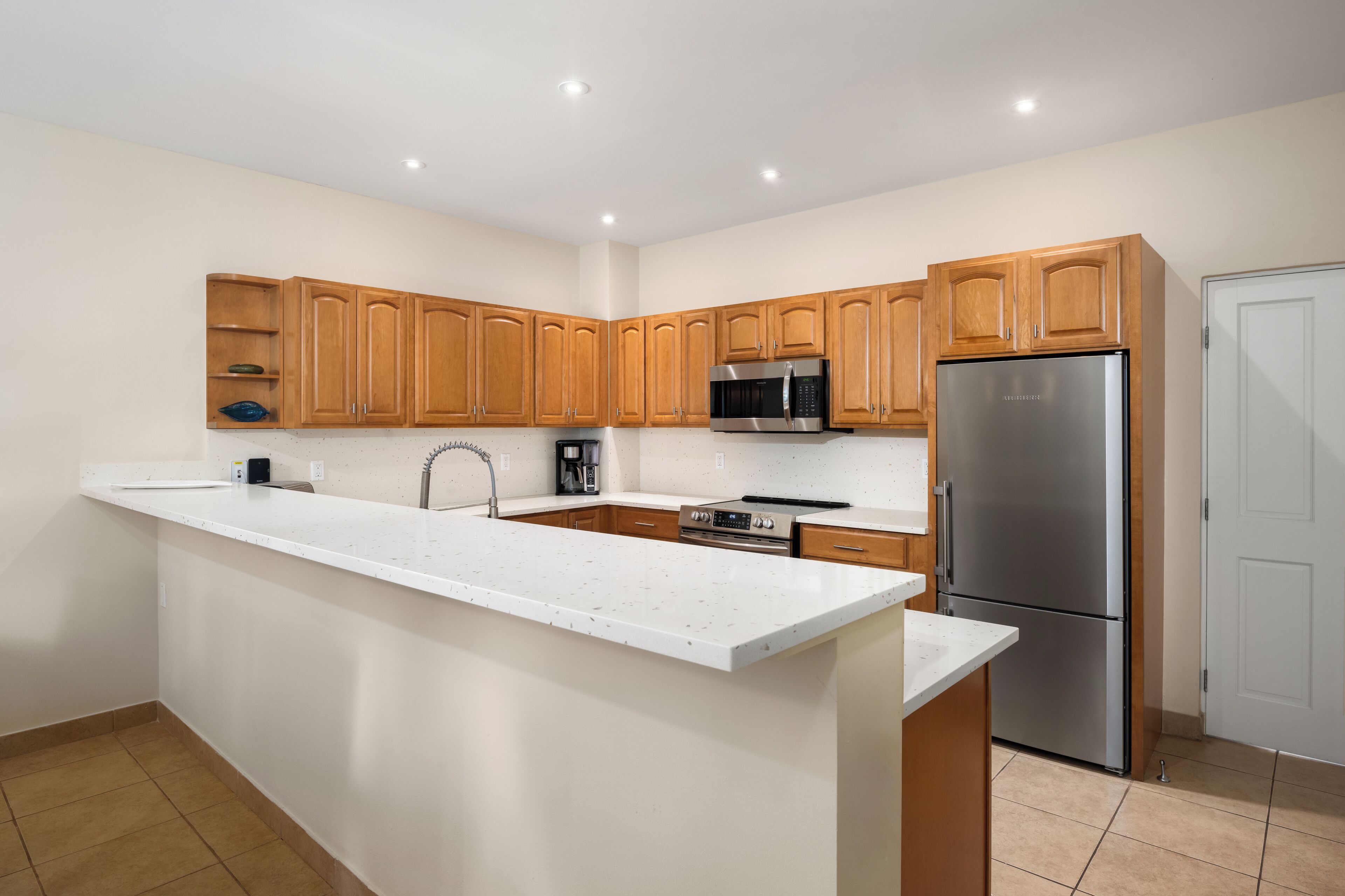 Una cocina moderna con armarios de madera, un refrigerador de acero inoxidable, un microondas y una isla grande con un lavamanos.