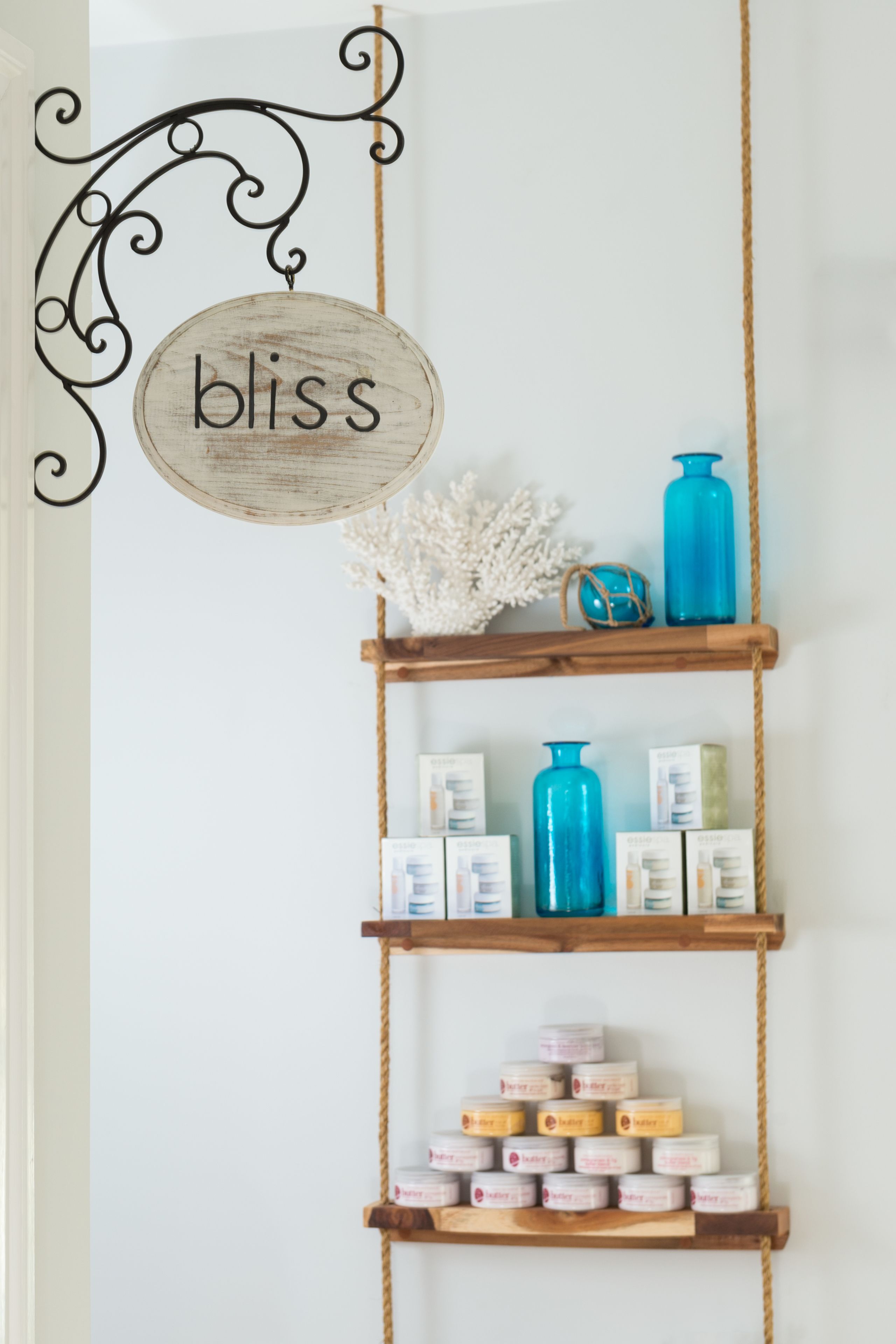 A wall with a wooden shelf holding various items, a sign with the word "bliss", and a decorative rope.