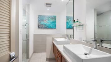 Une salle de bain moderne avec deux lavabos, une douche à l’italienne en verre et des œuvres d’art accrochées au mur.