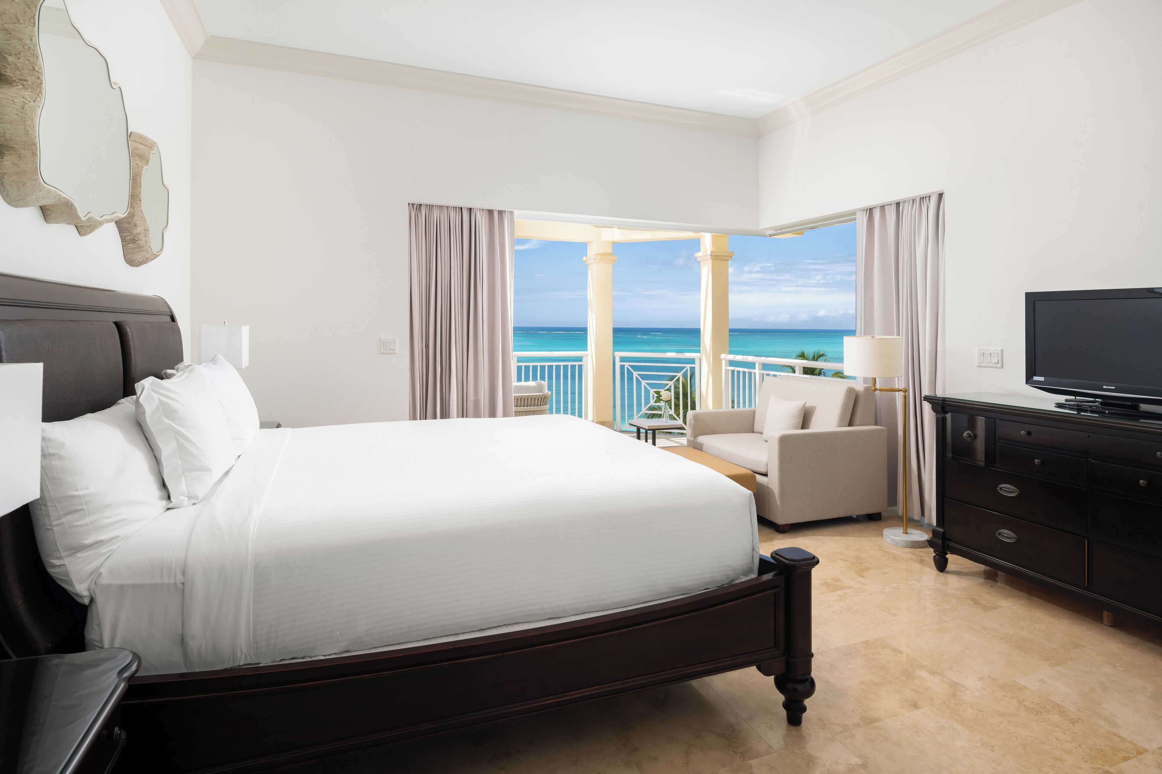 A hotel room with a large bed, a TV, a desk, and a view of the ocean.