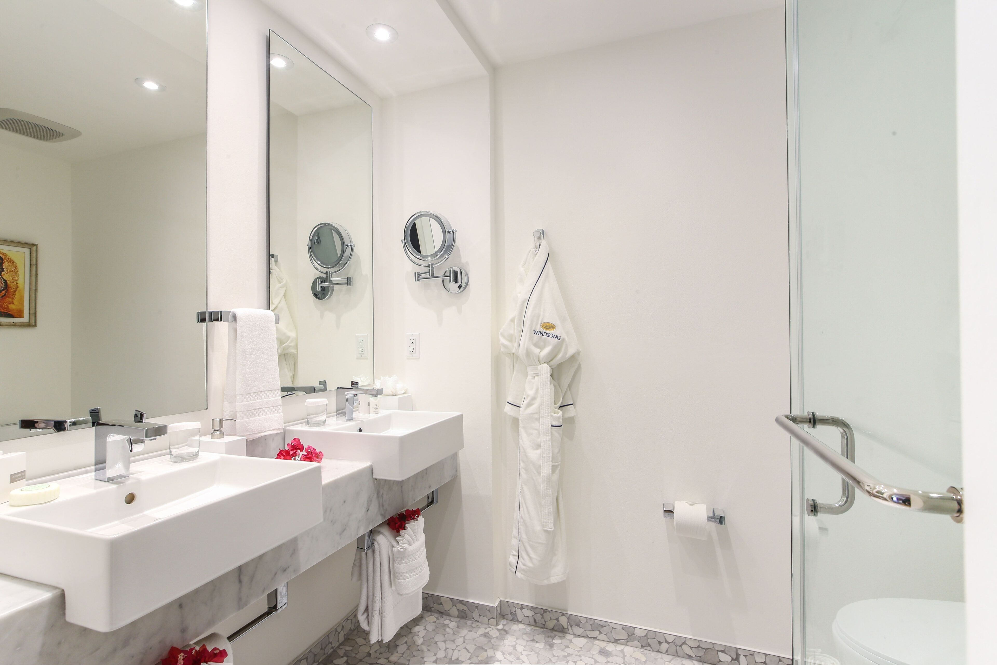 A modern bathroom with two sinks, a large mirror, a robe hanging, and a glass shower enclosure.