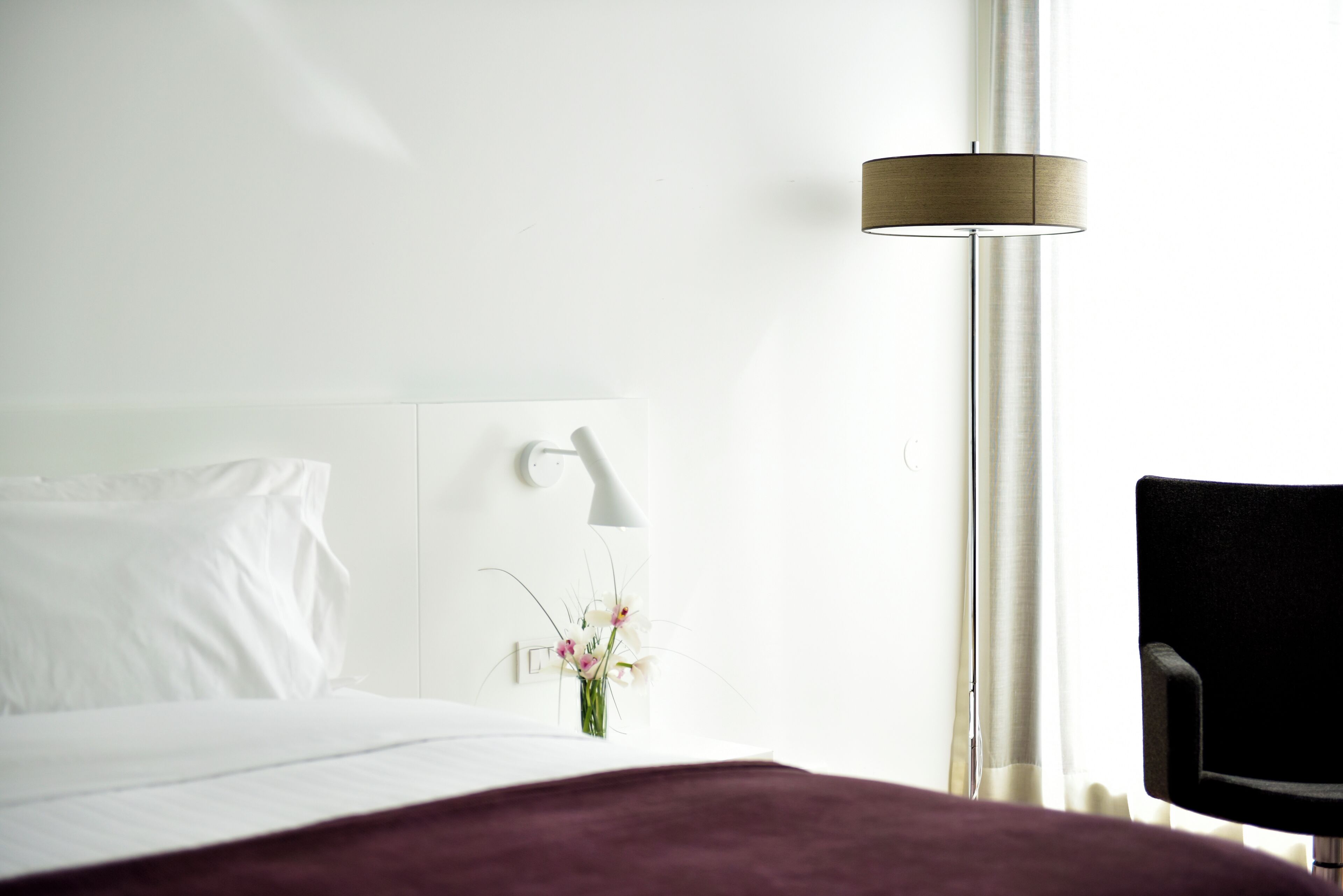 Ein Hotelzimmer mit Bett, Nachttisch, Lampe, Stuhl und einem Fenster mit Vorhängen.