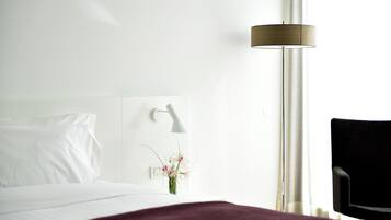 Ein Hotelzimmer mit Bett, Nachttisch, Lampe, Stuhl und einem Fenster mit Vorhängen.