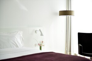 A hotel room with a bed, a nightstand, a lamp, a chair, and a window with curtains.