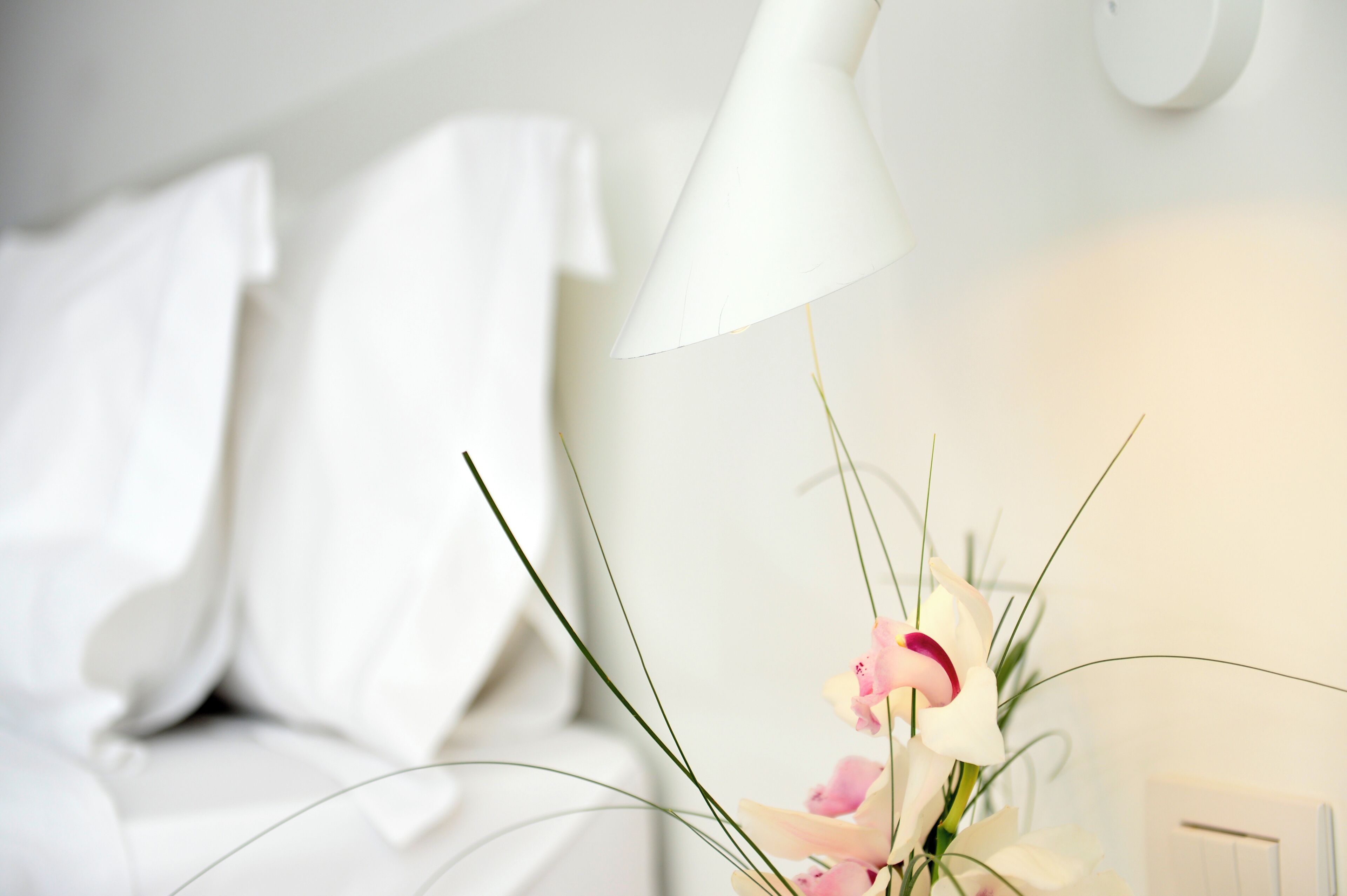 A neatly made bed with white linens and a white lamp beside it.