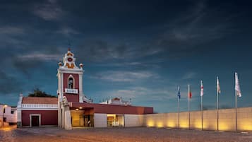 A historic building with a bell tower, a courtyard, and flags.