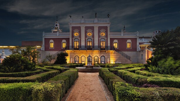 Un edificio imponente con fachada simétrica, una fuente central y un jardín formal.