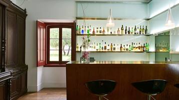 A bar area with wooden cabinets, a glass shelf with bottles, and two black bar stools.